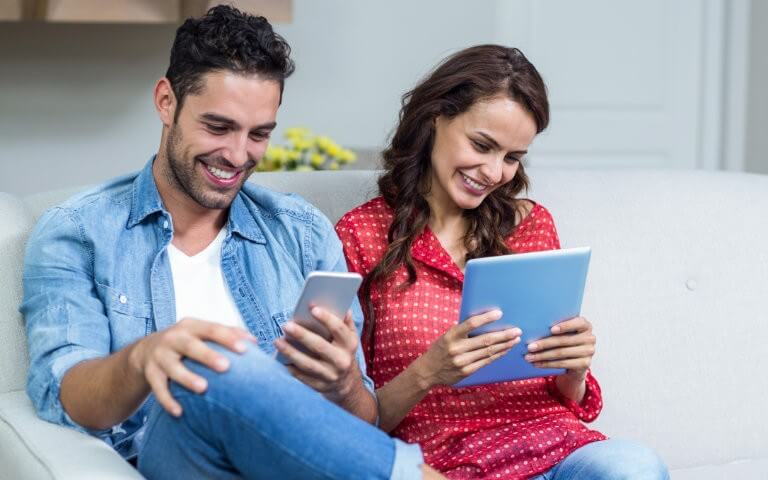 Happy couple using smartphone and tablet to read ebooks