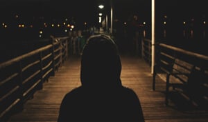 Hooded person walks on boardwalk at night.